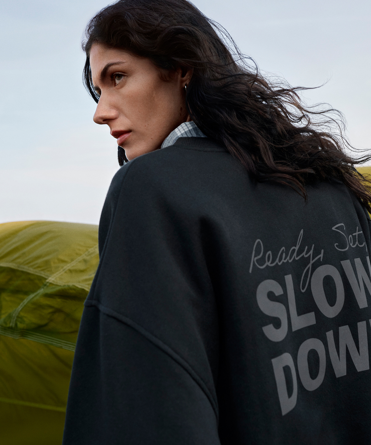 Dark oversized sweatshirt featuring 'Slow Down' on the back, worn outdoors.
